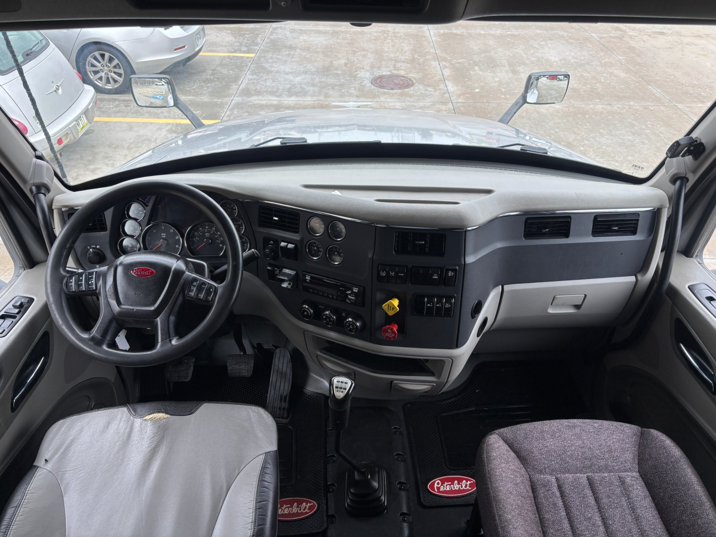 Peterbilt 579 cab interior view showing steering wheel, dashboard controls, gear shifter, and driver's seat with Peterbilt logos.