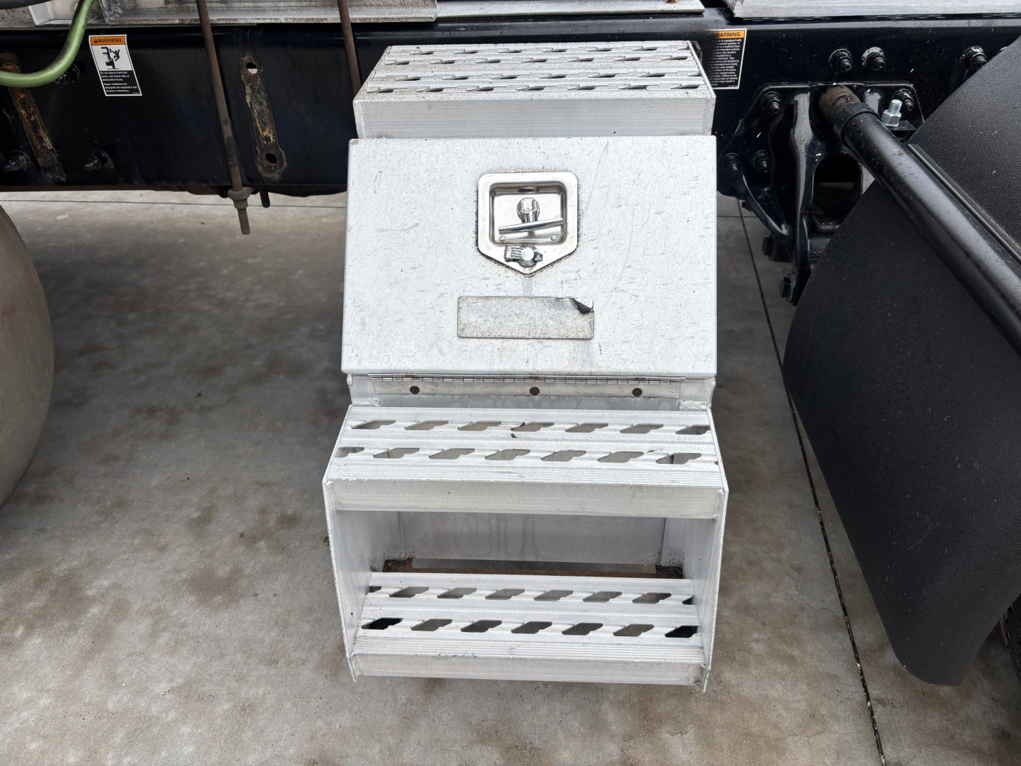 Truck side view showing aluminum side steps with metallic housing and steps; small emblem on top box with square logo; undercarriage details visible.
