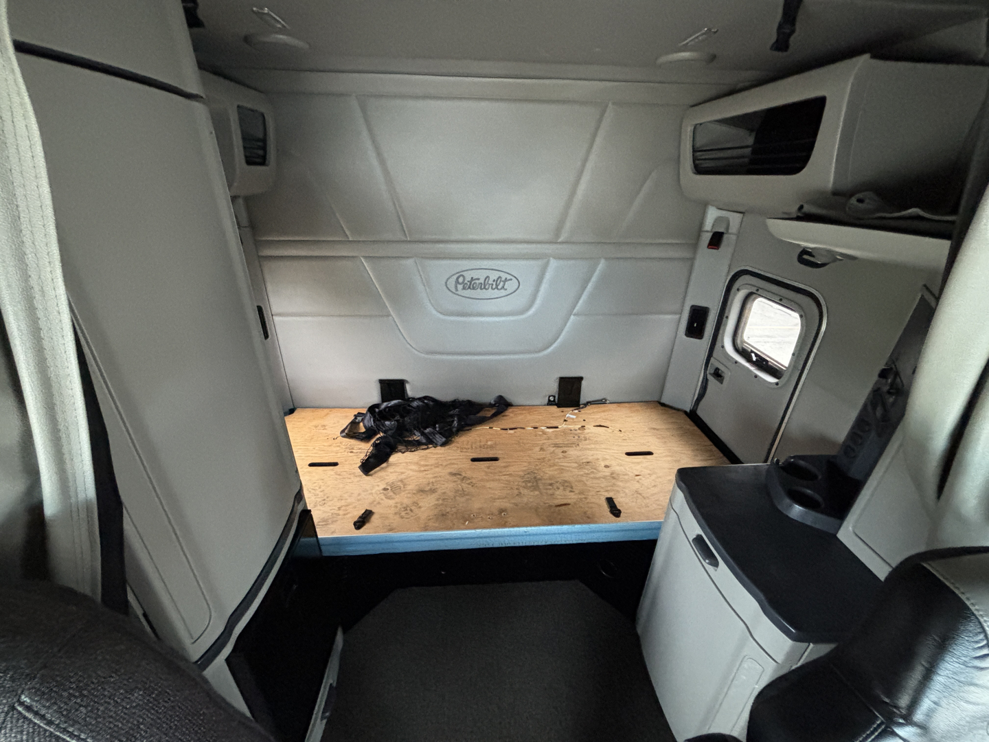 Peterbilt sleeper cab interior showing cargo area and side wall with Peterbilt emblem, window, and storage cabinets.