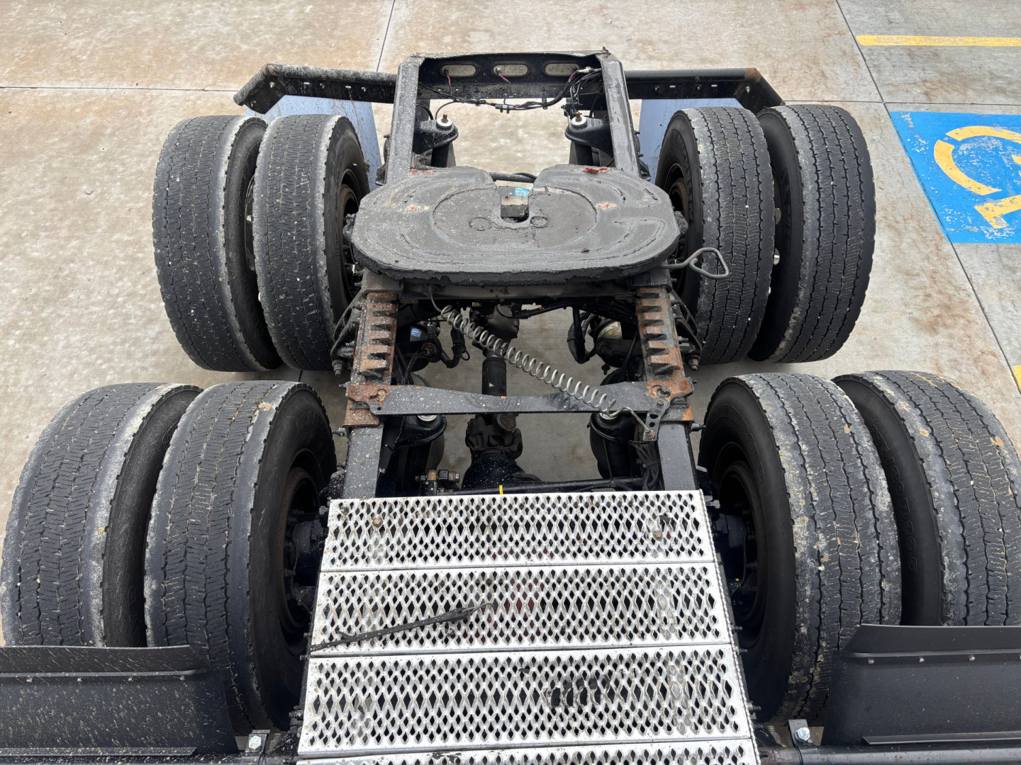Peterbilt truck chassis showing dual rear axles and fifth wheel hitch with metal step; six wheels visible with tires and suspension components.