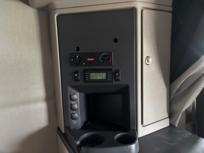 Peterbilt 579 truck interior dash center console view showing control panel with 12V/AC gauges and a radio display, cup holders, and storage area.