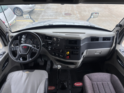 Peterbilt 579 cab interior view showing steering wheel, dashboard controls, gear shifter, and driver's seat with Peterbilt logos.
