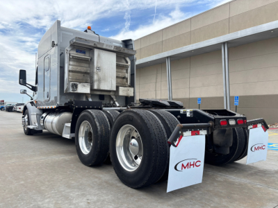 Peterbilt 579 truck rear view showing dual rear axles with mud flaps and chrome fuel tanks; sleeper cab with external exhaust; no license plate visible.