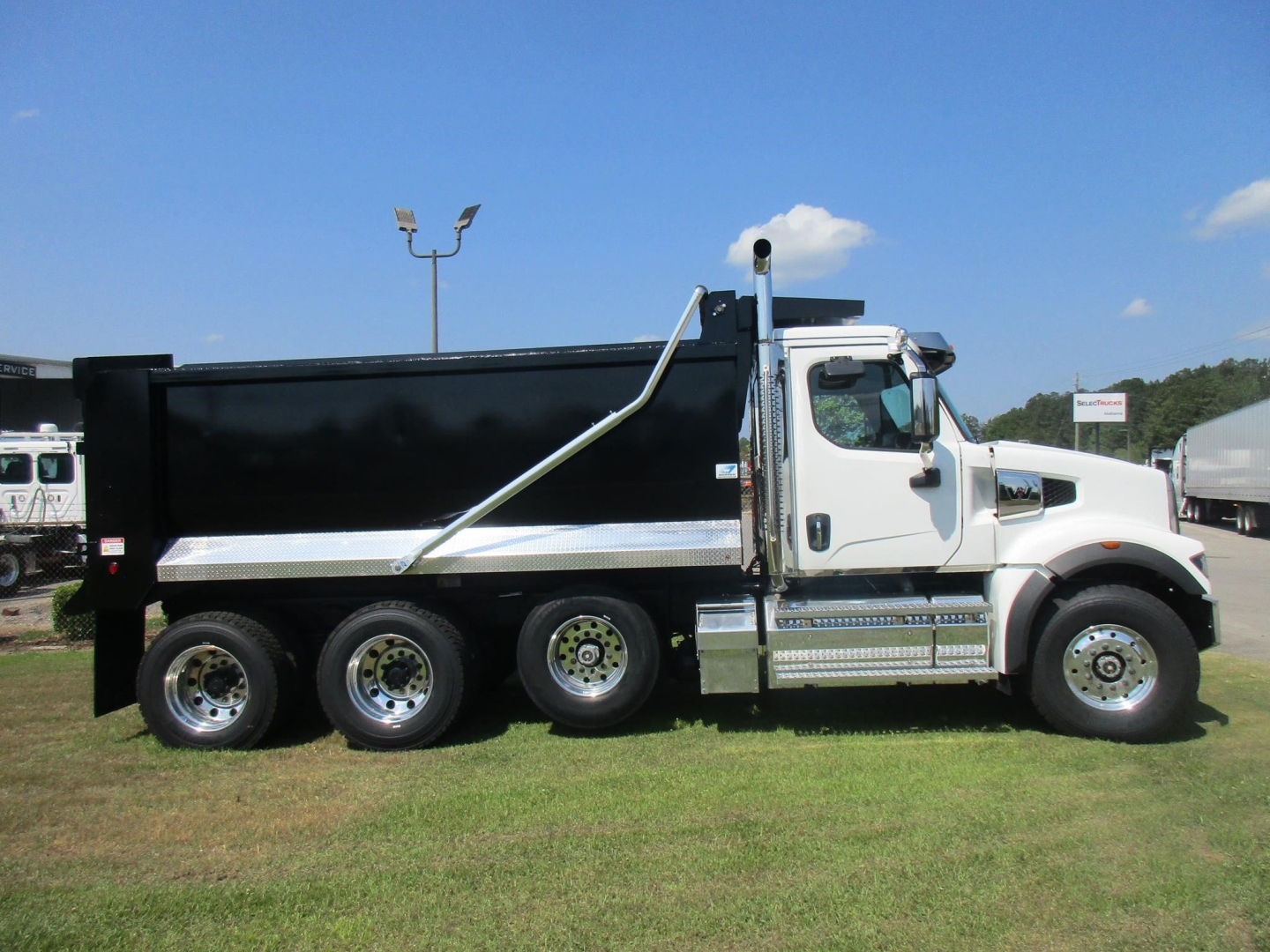 Dump truck with white cab and black dump body, three-axle configuration, side view showing chrome mirrors and steps.