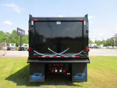 Dump truck rear showing black cargo bed with blue and white Warren mud flaps and taillight assembly, reflecting a sunny day.