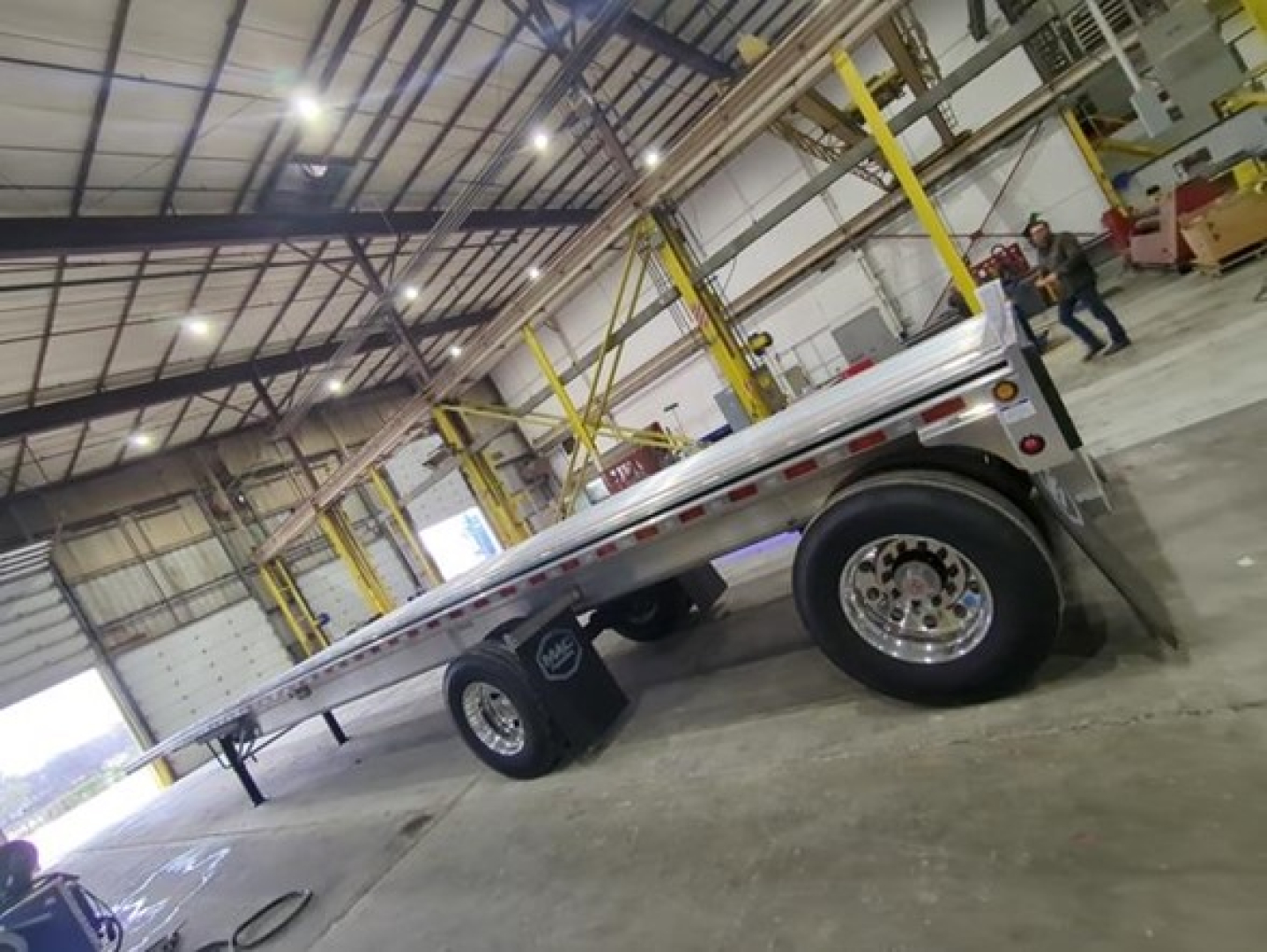 Flatbed trailer inside a warehouse showing aluminum deck and dual rear wheels with chrome rims.