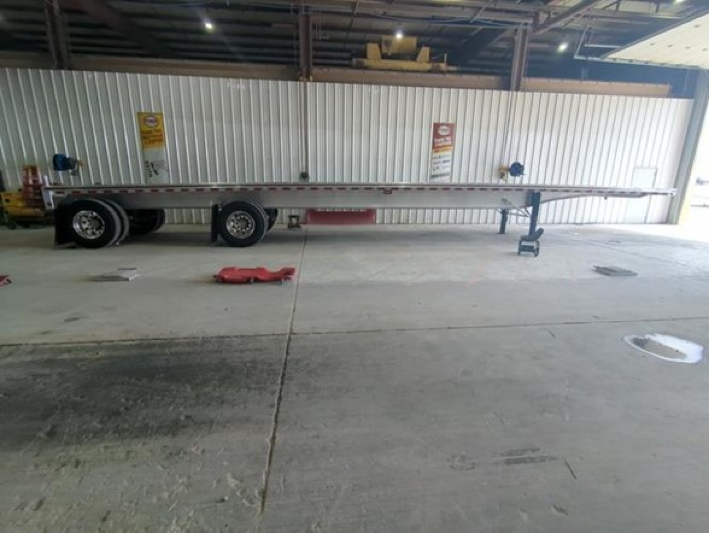 Trailer chassis and flatbed showing long steel frame and dual rear axles, Pip warning signs on wall, tag and wheel spare visible.