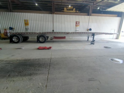 Trailer chassis and flatbed showing long steel frame and dual rear axles, Pip warning signs on wall, tag and wheel spare visible.