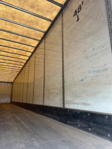 Interior of a 2014 Wabash trailer with aluminum walls, wooden floor, and black base trim. Markings '48' on side wall and blue repair marks along panel.