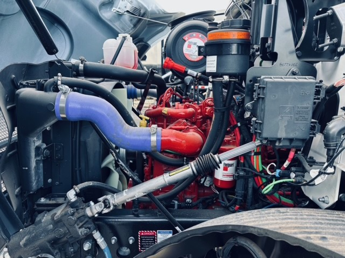 Mack MD6 engine bay with red engine block, blue coolant hose, black hoses, and various components visible.