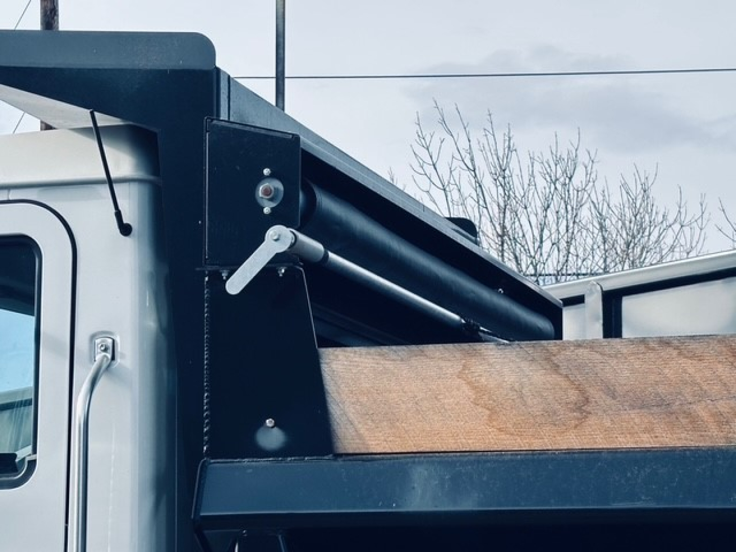 Truck bed side showing hydraulic hoist mechanism and dump bed edge on Mack MD6, with metal frame and wood side panel.