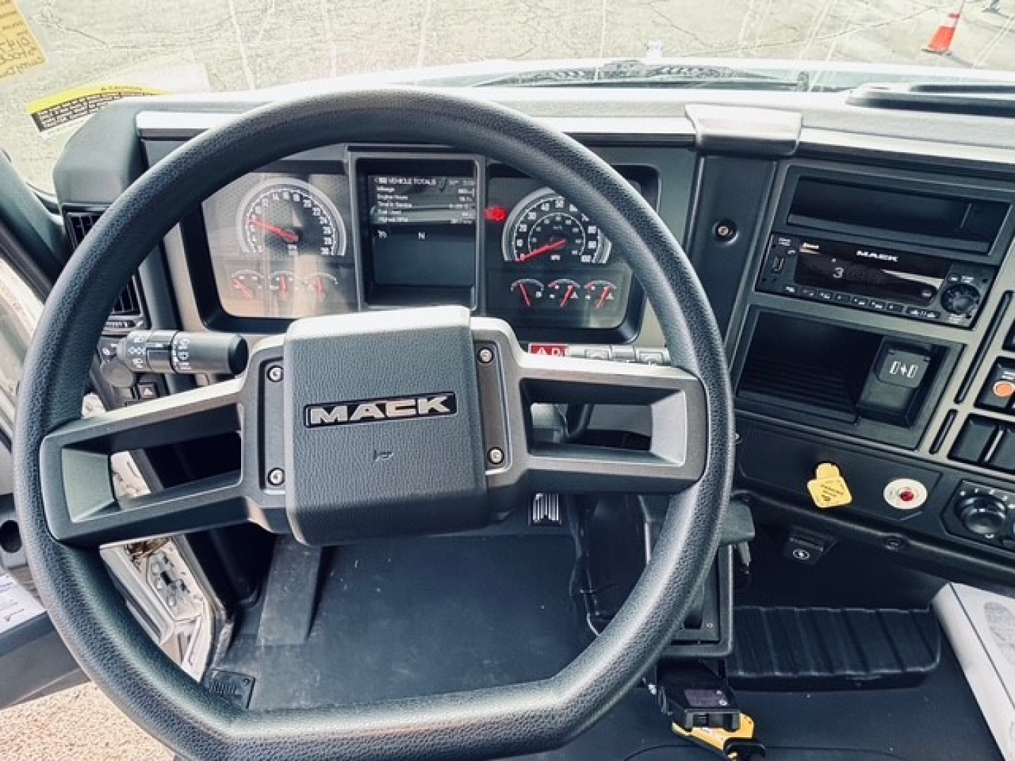 Mack MD6 cab interior showing steering wheel with MAEK logo, instrument cluster, dashboard controls, and radio/display panel.