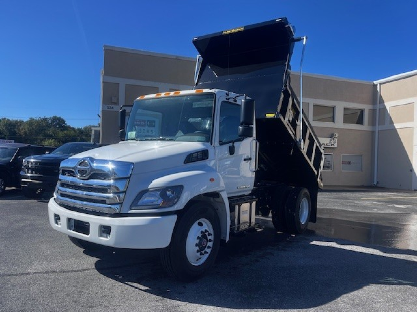 2026 Hino L7 dump truck with hydraulic dump bed raised, front grille, white cab, side mirrors, and dual rear wheels.
