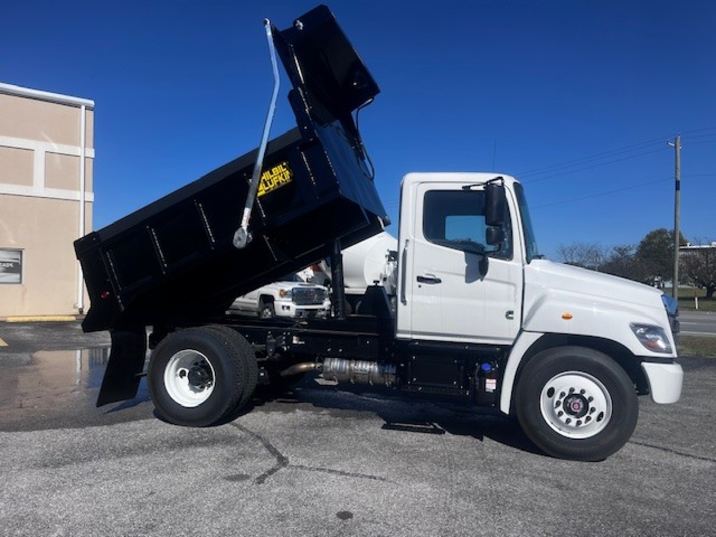 Truck cargo dump body on white cab with raised black dump bed in a parking lot.