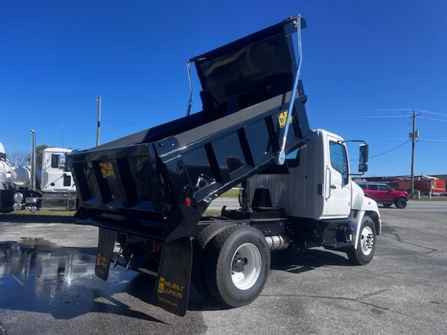 Truck dump body on a white cab, rear dump bed raised, side view showing hydraulic lift and dual rear wheels.