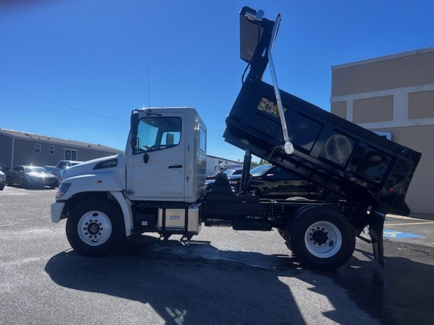 New 2026 Hino L7 dump truck side view with bed raised, white cab, black dump body, stock #68900, VIN visible.