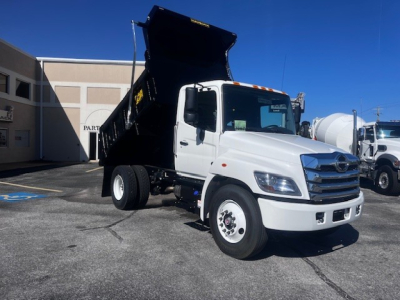 White 2026 Hino L7 dump truck with open dump bed, front view showing cab and raised bed. Text on truck not legible.