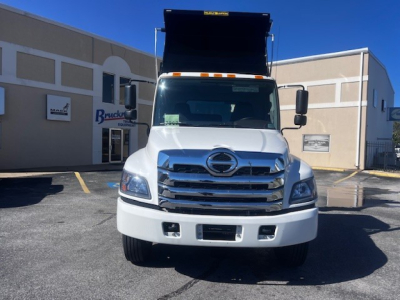 Front view of a white Hino dump truck with raised dump bed, chrome grille, and large bumper. Vehicle appears in a dealership lot.