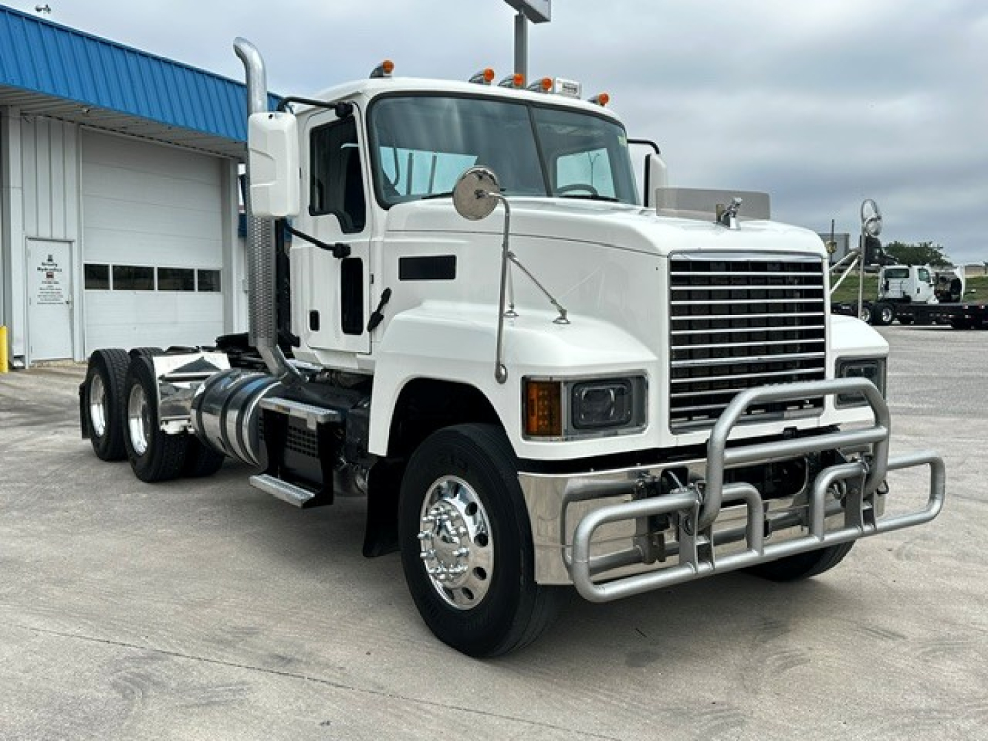 Truck engine bay view showing 2020 Mack PI64T conventional daycab with grille, bumper guard, dual rear axles, and chrome wheels.
