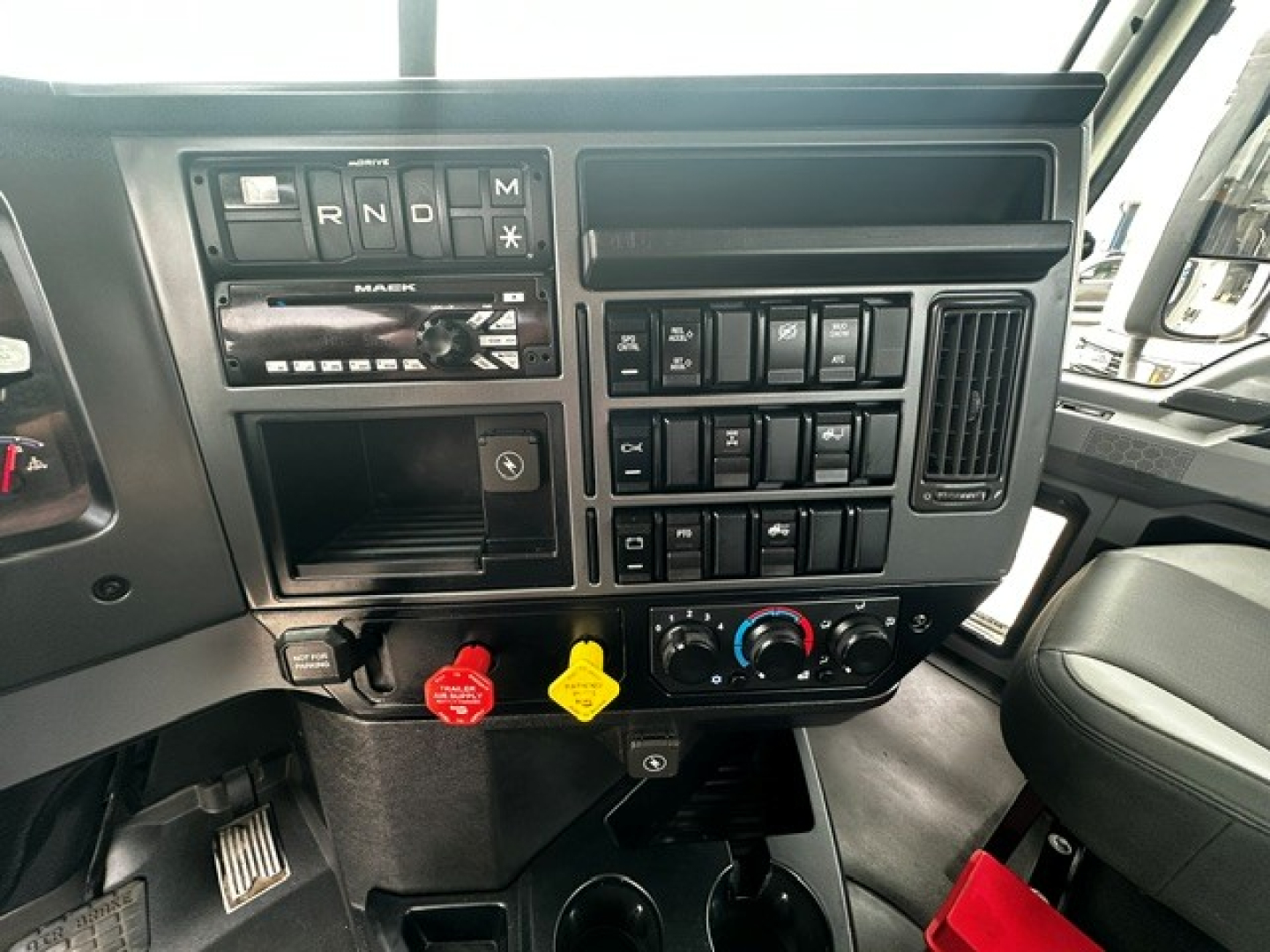 Mack PI64T dash area showing controls and climate vents; includes red and yellow knobs, radio/navigation slot, numerous switches, and steering column visible.