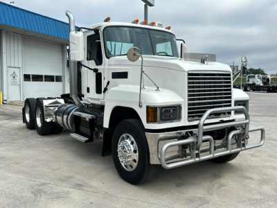Truck engine bay view showing 2020 Mack PI64T conventional daycab with grille, bumper guard, dual rear axles, and chrome wheels.
