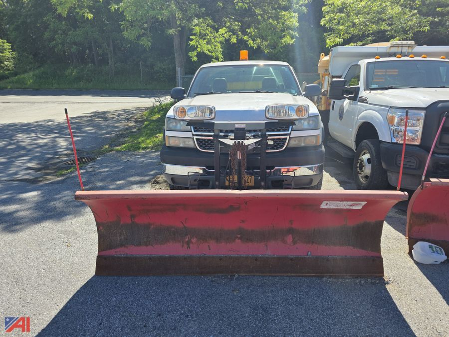 Chevrolet Silverado 2500HD pickup with front-mounted plow on a gravel lot, two utility trucks in background.