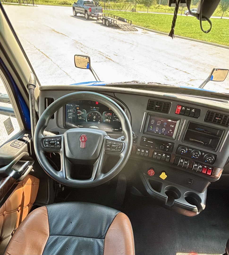 Kenworth T680 cab interior with steering wheel, dashboard, and center console showing gauges and control buttons.