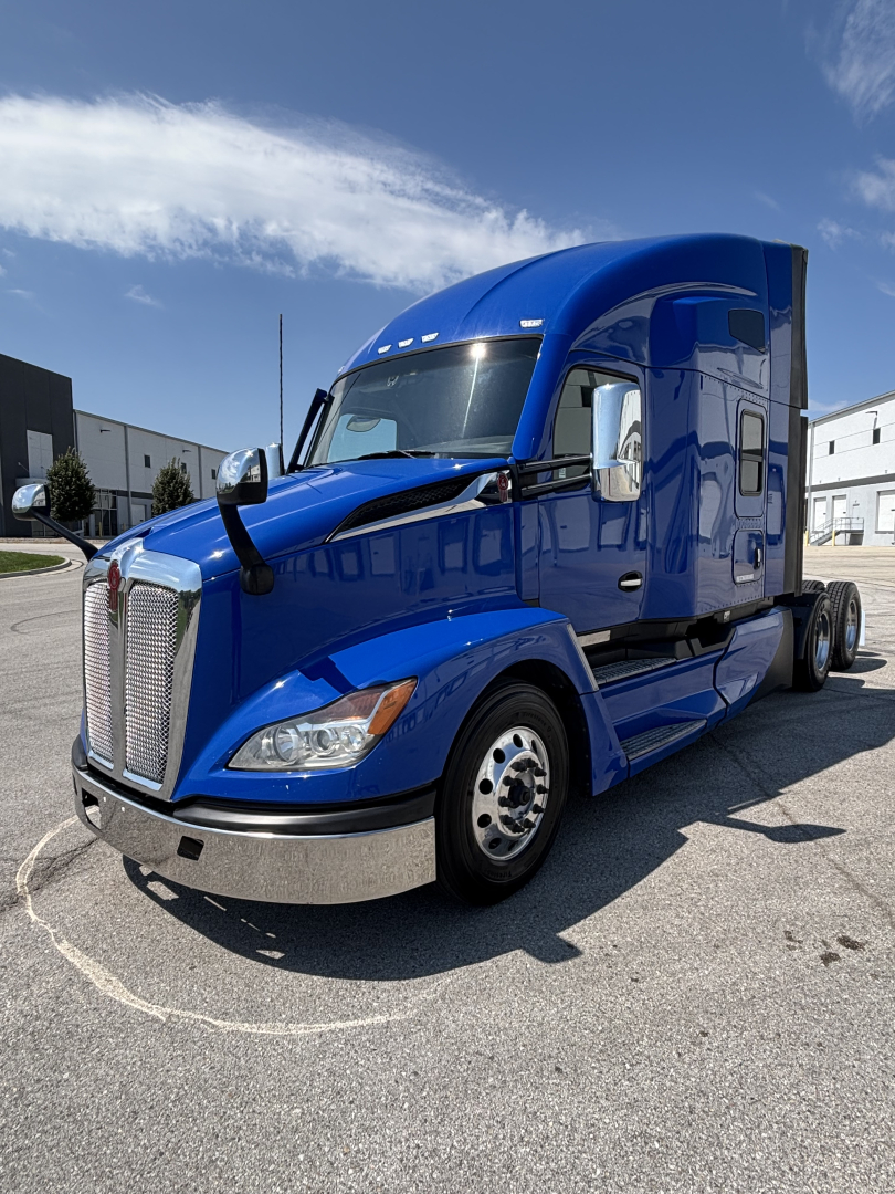 Blue 2023 Kenworth T680 semi-truck tractor cab, front-left view with chrome grille and side mirrors.