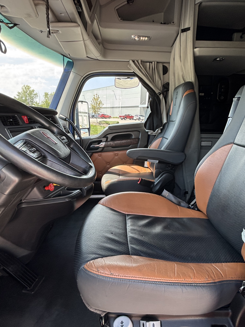 Kenworth T680 truck interior showing driver and passenger seats in brown and black leather, steering wheel, and dashboard with overhead storage and curtain in view.