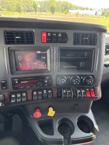 Kenworth T680 cabin dashboard with central touchscreen display, multiple control switches, climate controls, cup holders, and yellow and red ignition keys visible.
