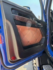 Kenworth T680 door interior panel with brown quilted leather insert and chrome trim seen from open cab door.