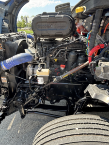 Kenworth T680 engine bay with visible air filter housing labeled PACCAR and various hoses, wiring, and components in view.