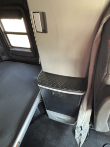 Kenworth T680 interior showing a knee area with a diamond-pattern black step and a small storage compartment under a vertical cabinet, part of the sleeper cab interior.