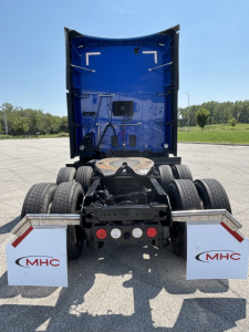 Rear view of a blue Kenworth T680 tractor with dual rear wheels and mud flaps, showing chassis and fifth wheel area.