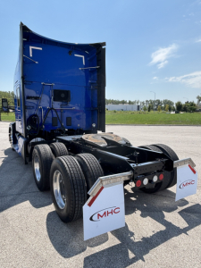Kenworth T680 tractor rear view showing fifth wheel, dual rear axles, and mud flaps with MHC logos.