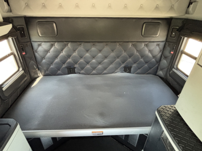 Truck sleeper cab interior with quilted black padding on walls, small rectangular windows on sides, and a flat bed platform; visible text includes VIN and stock details from listing.