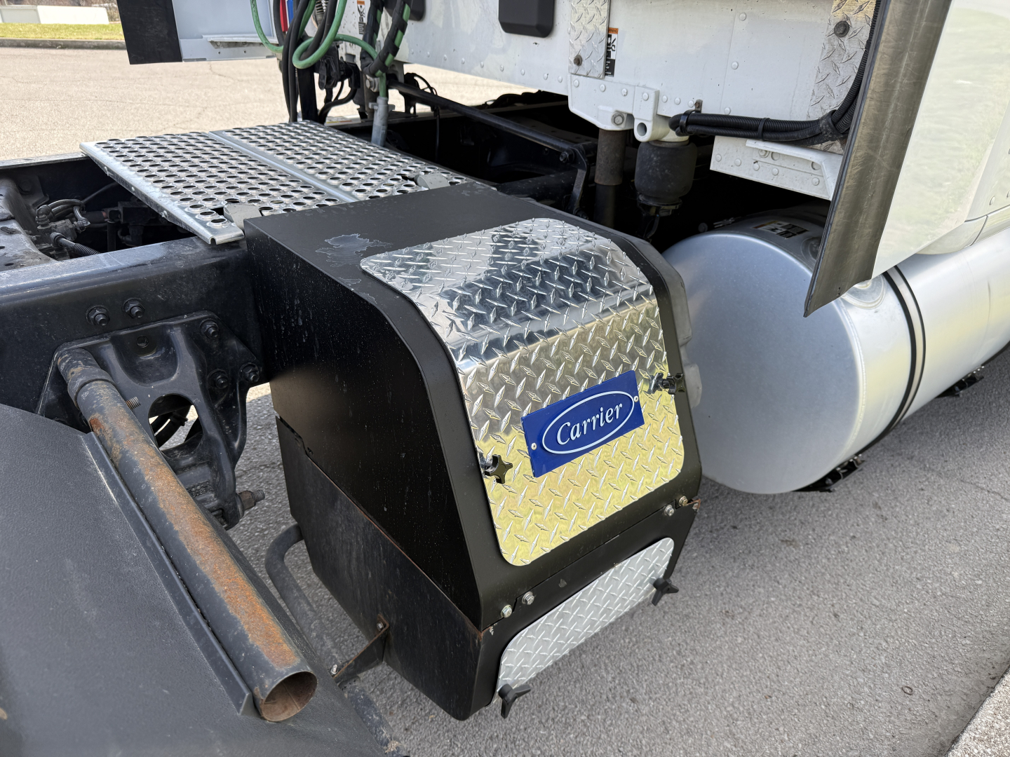 Truck rear view showing Carrier A/C or auxiliary unit with diamond plate access cover and steps on a Kenworth T680. Side fuel/air tanks visible.