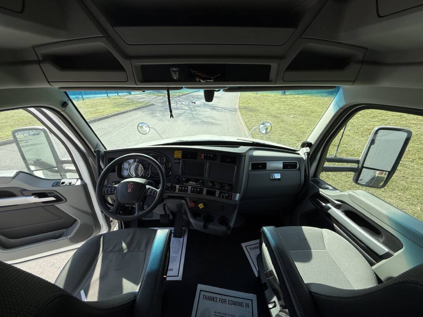 Kenworth T680 cab interior showing steering wheel, dashboard, driver and passenger seats, front windshield and side mirrors.