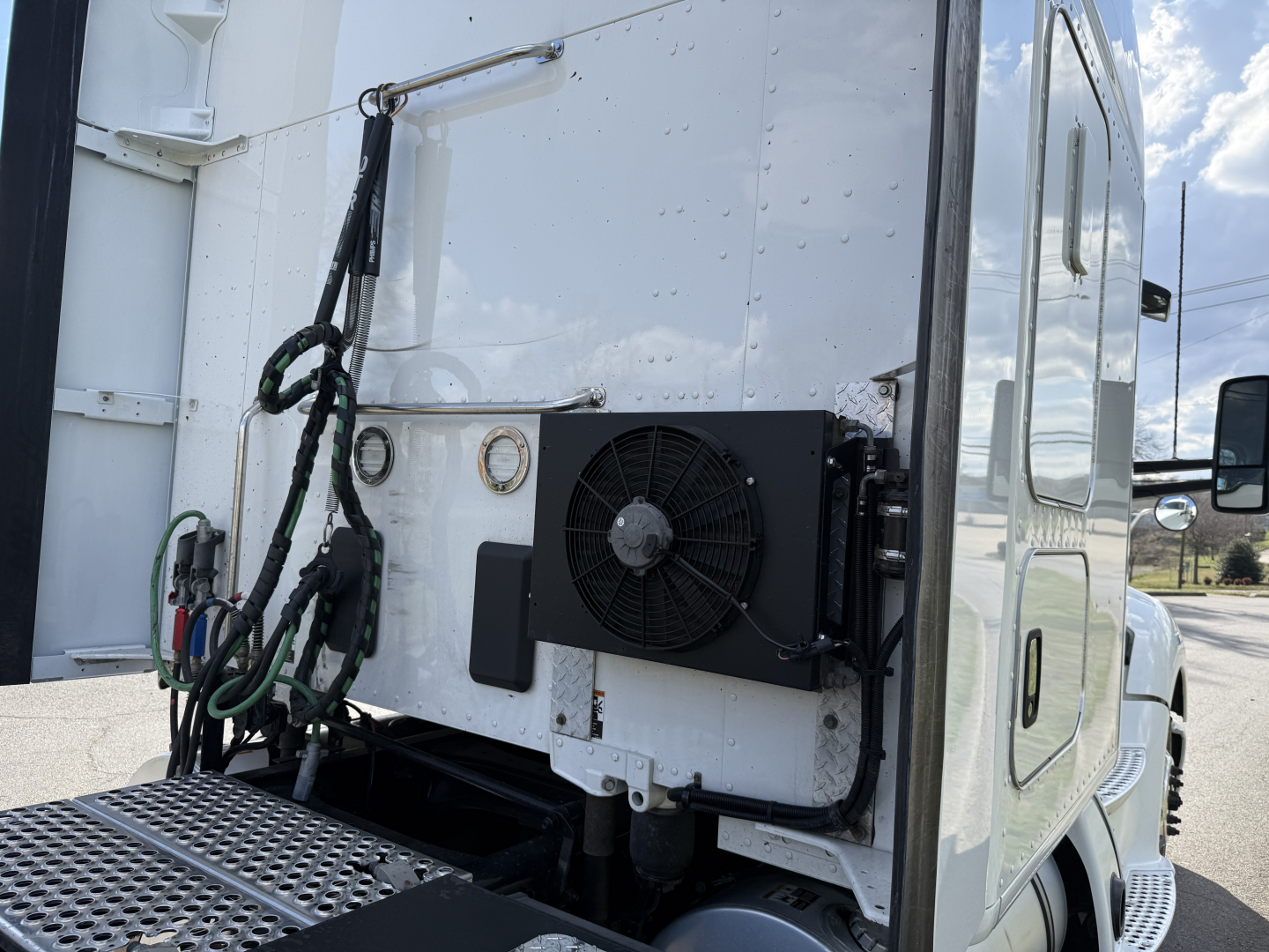 Kenworth T680 rear cab area showing cooling condenser/fan assembly mounted on white truck body with cables and hoses nearby.