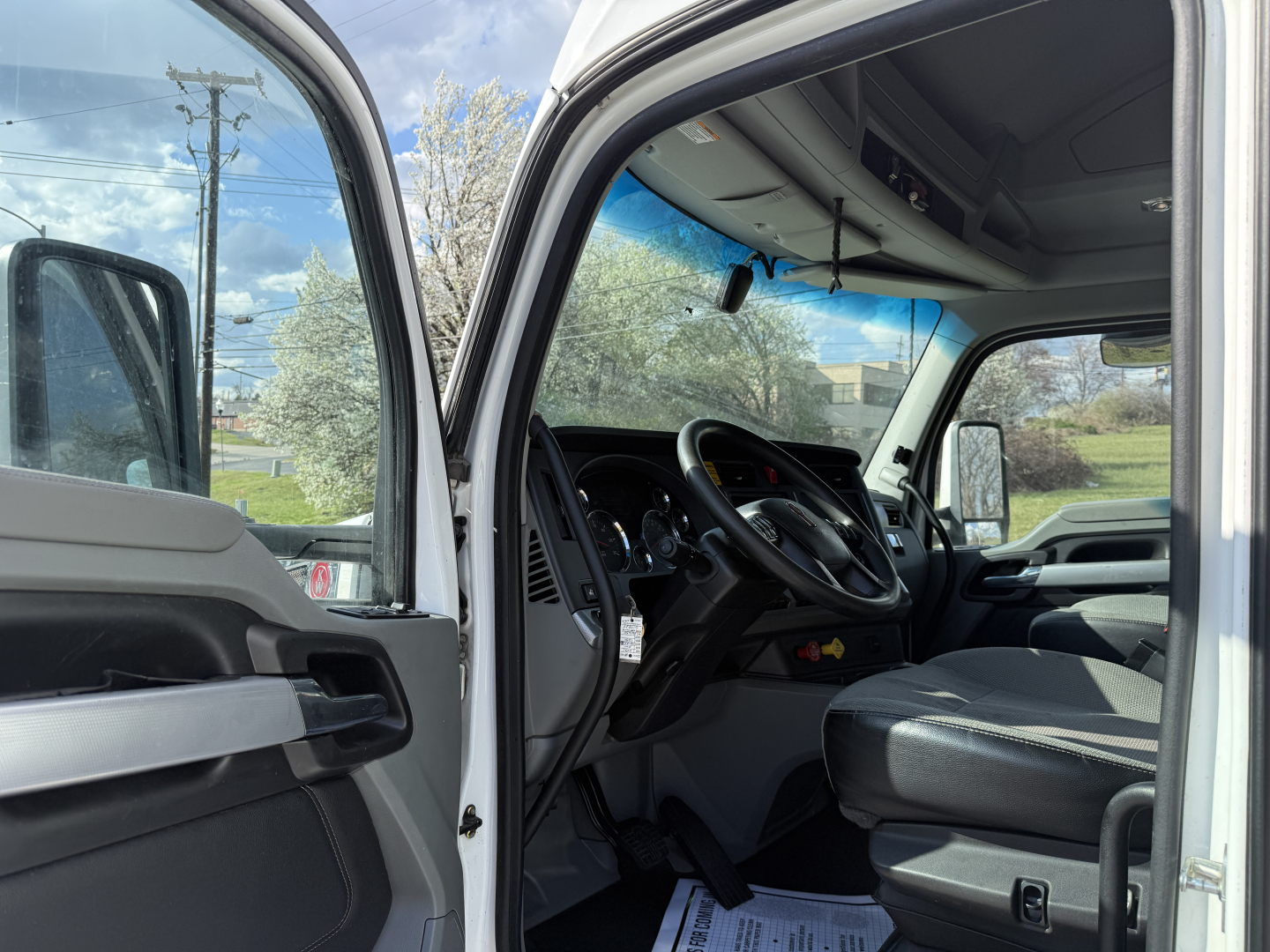 Kenworth T680 truck interior view from open driver-side door showing steering wheel, dashboard, and front seat