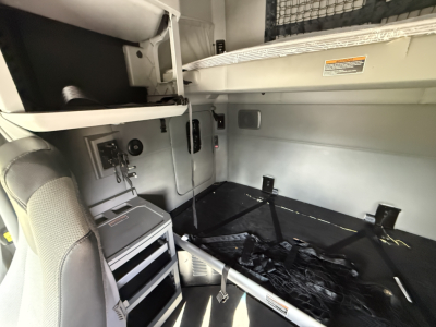 Interior sleeper area of a 2021 Kenworth T680 with storage compartments, seat, and cargo net in view.