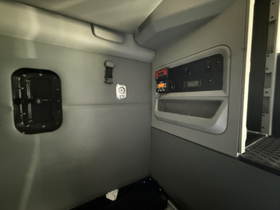 Interior of a used 2021 Kenworth T680 cab area showing side panel with switches, a small window hatch, and a control panel/seat area.