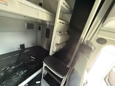 Truck cab interior showing storage compartments and a step with textured surface near a partition; faint control panel and wiring visible.