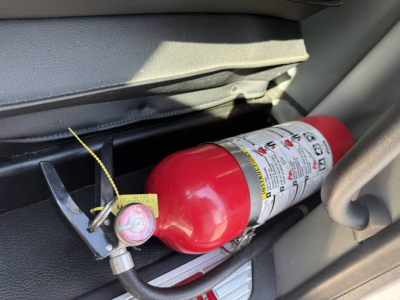 Fire extinguisher mounted inside Kenworth T680 cab with label and mounting bracket visible.