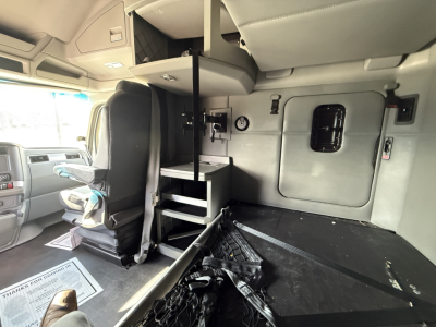 Cab interior of a 2021 Kenworth T680 showing sleeper area with ladder, storage compartments, and driver seat.