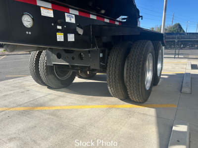 Dump trailer undercarriage with dual axles and tires, black frame, various labels and stickers visible on side of the trailer.