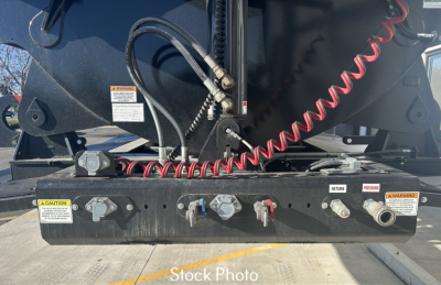 Industrial trailer hitch area with control panel and hydraulic lines; multiple valves and warning labels visible.