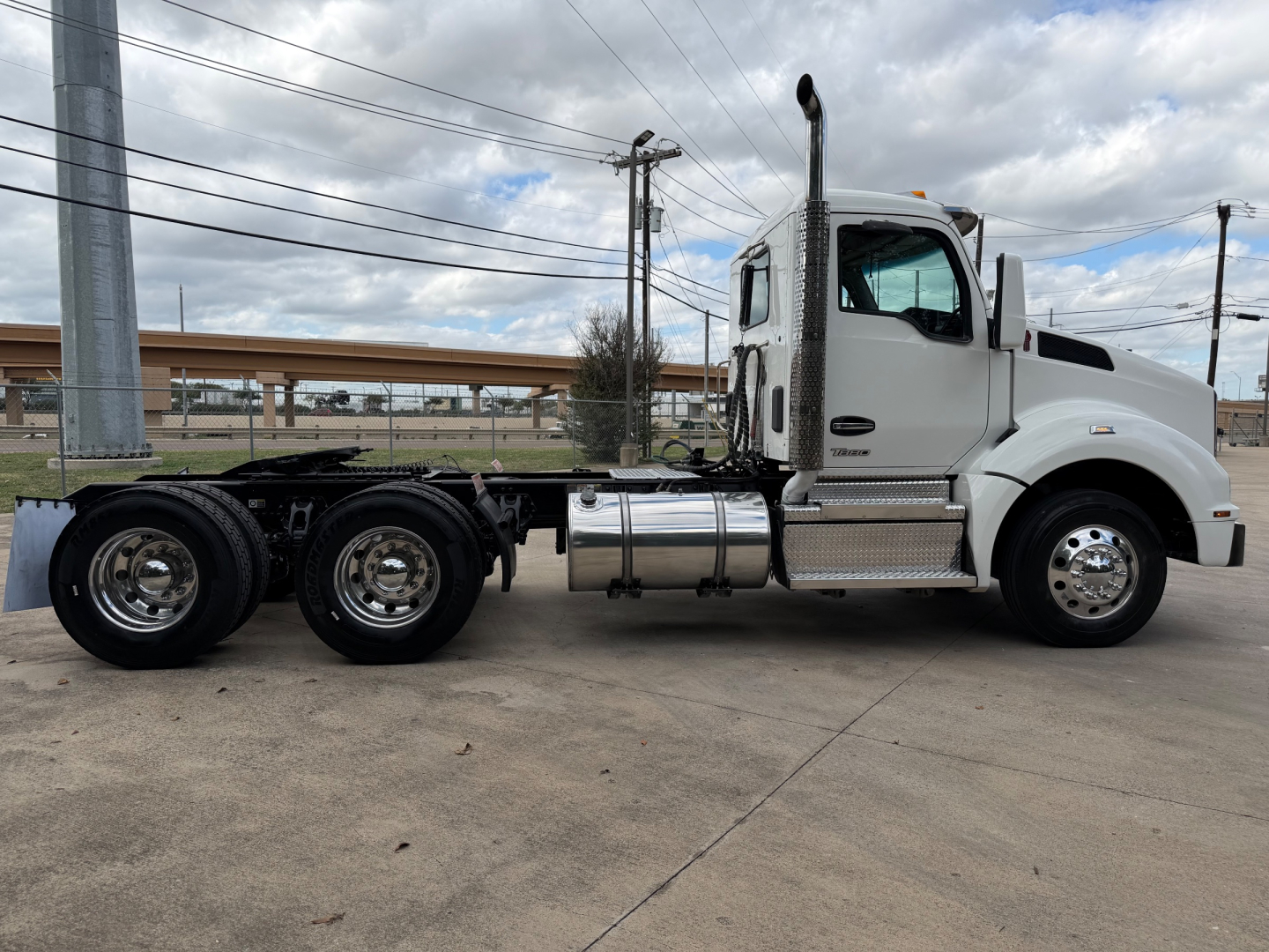 Kenworth T880 daycab tractor tractor-side view showing white cab, fuel tanks, exhaust stack, and dual rear axles on a concrete lot.