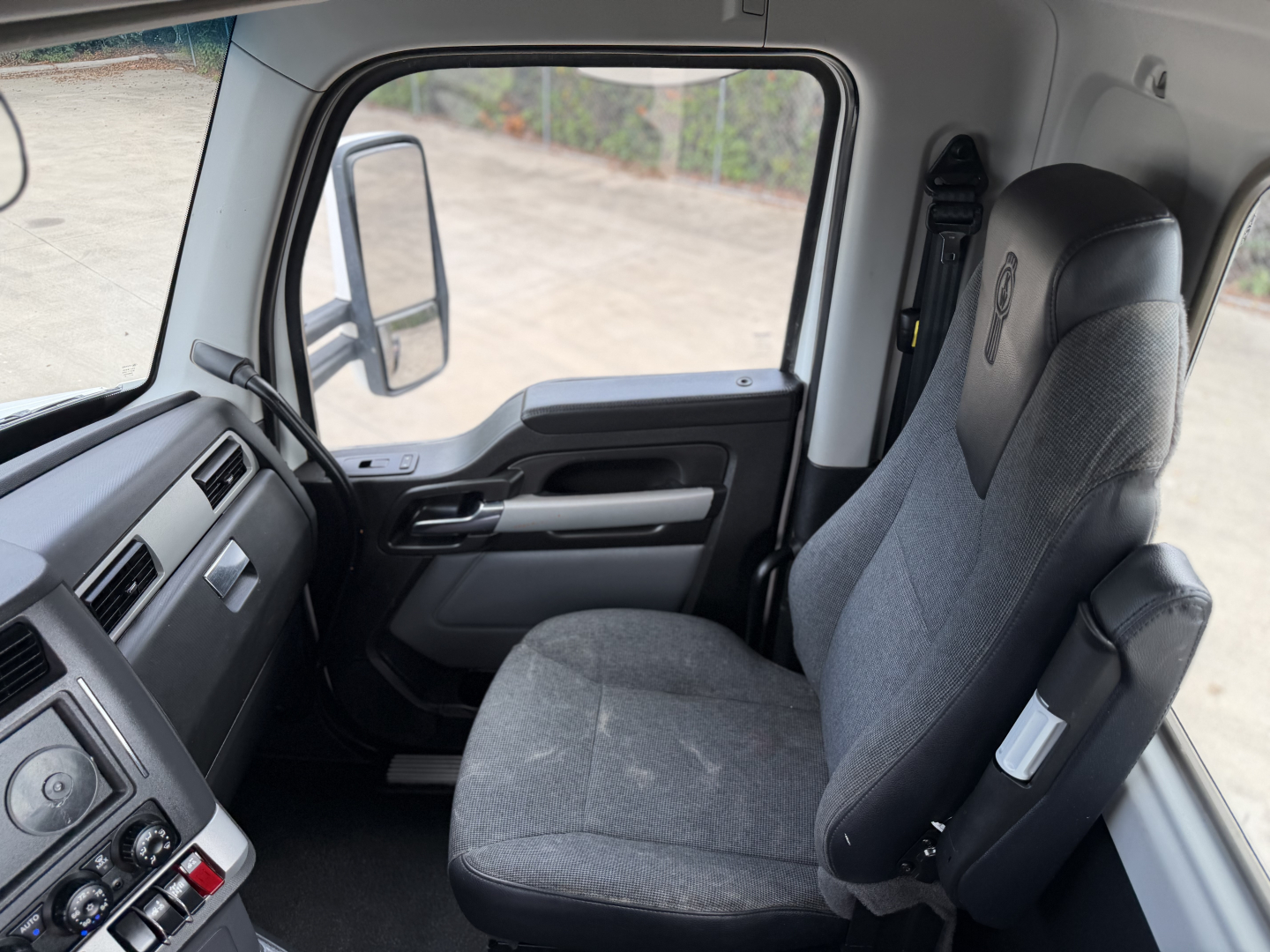 Truck cab interior view of a Kenworth T880 (driver seat and dashboard) with steering wheel, control panel, and side window.