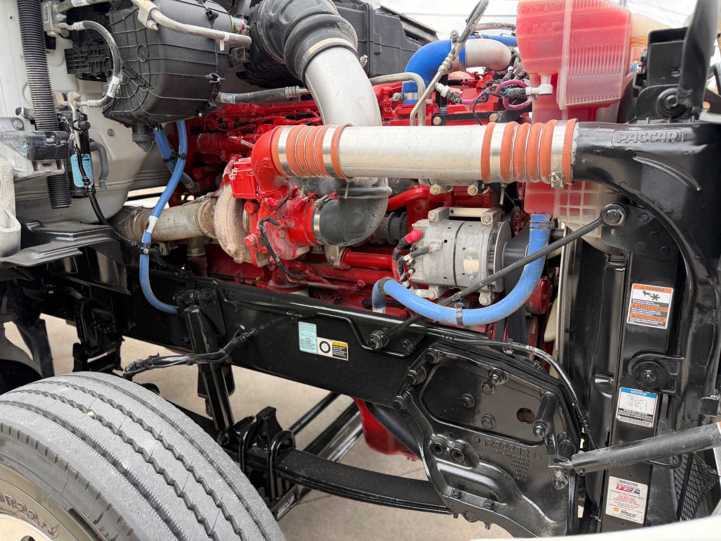 Kenworth T880 engine bay with red V8 diesel engine, blue hoses, and exposed frame showing components and coolant reservoir.